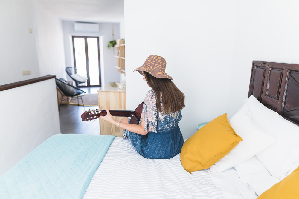 1754990354-rear-view-woman-sitting-bed-playing-guitar_(1).jpg
